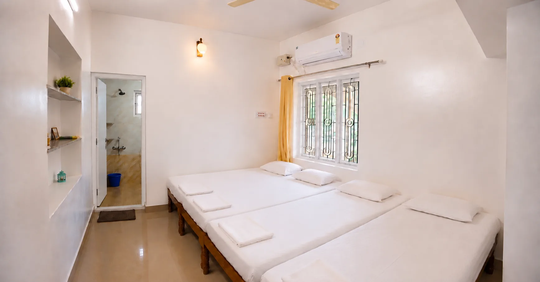 Bedroom with adjacent beds, air conditioner and bathroom doorway in Nidhi apartment.