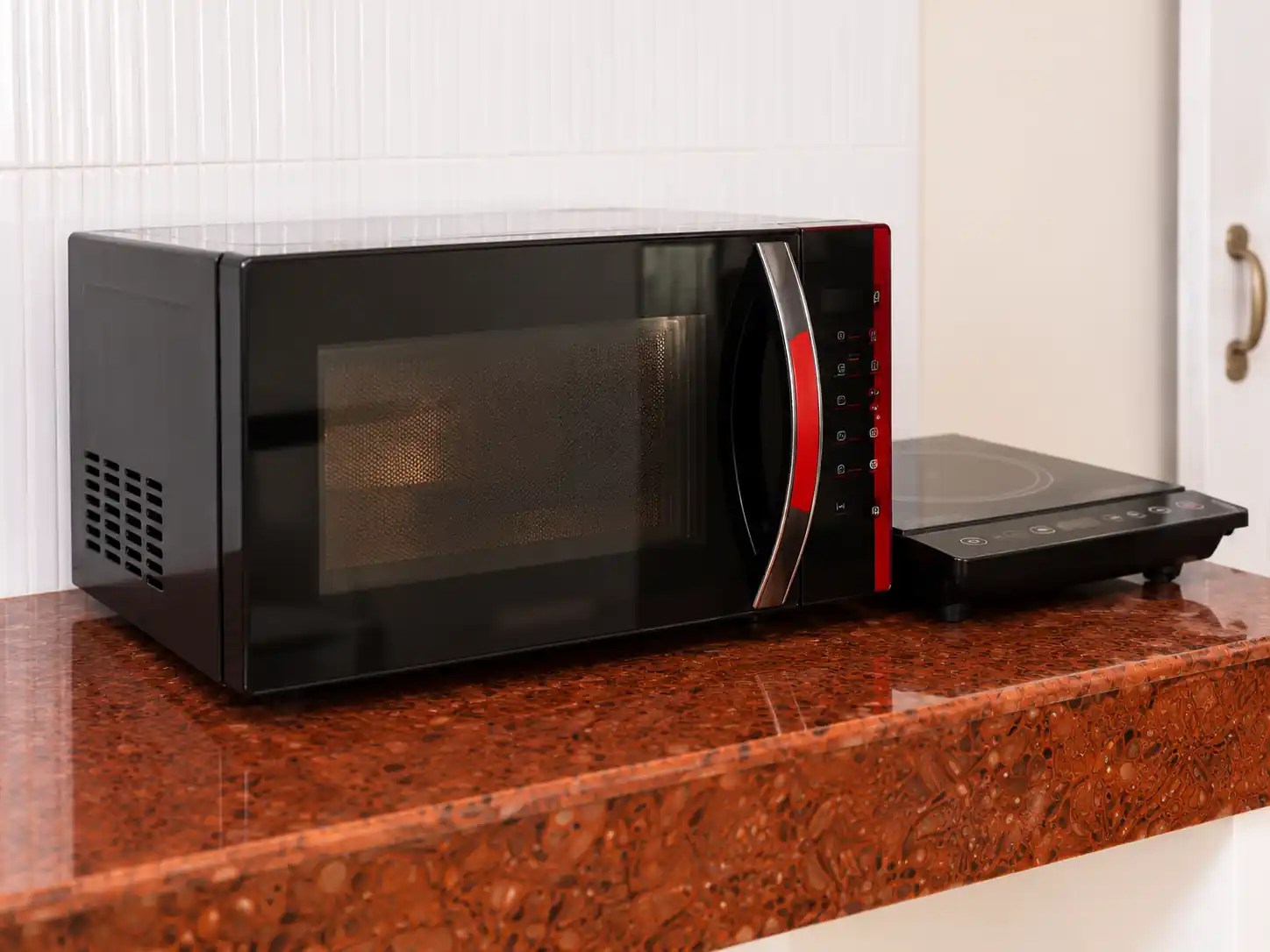 Microwave oven and induction cooktop in the Nidhi apartment kitchen at Balakrishna Udupi Homestay.