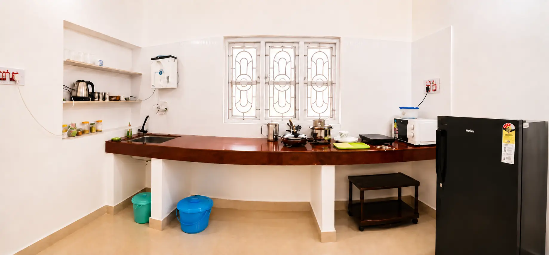Wide kitchen counter, window, cookware, appliances and refrigerator in SriNidhi apartment.