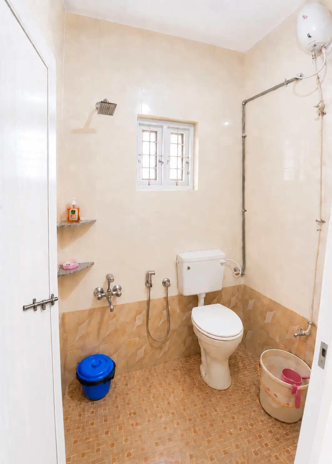 Portrait bathroom with toilet, shower fittings, heater and window in Nidhi apartment.