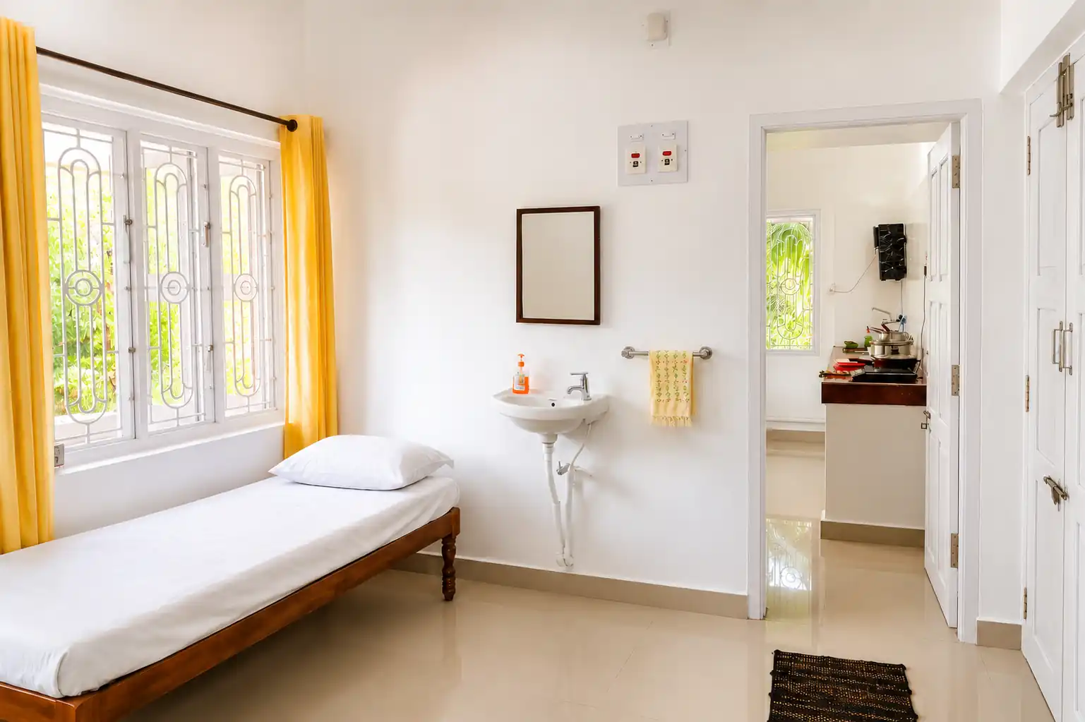 Single bed, washbasin, mirror and kitchen doorway in Nidhi apartment.