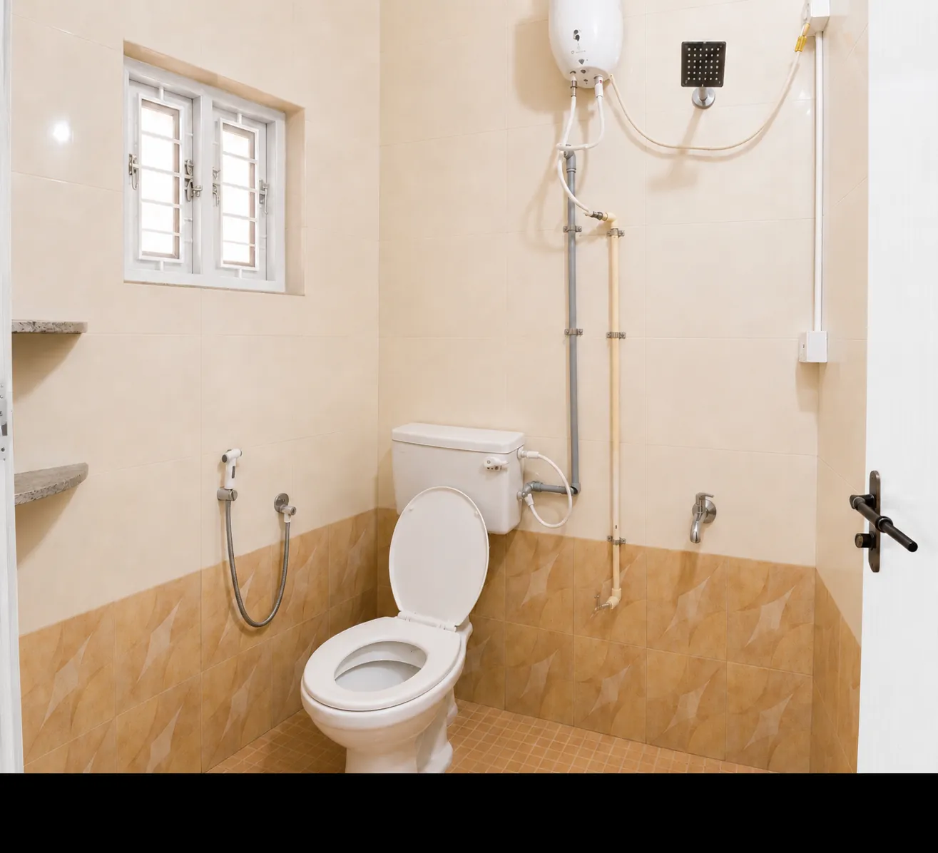 Bathroom with toilet, heater, shower fittings and window in SriNidhi apartment.