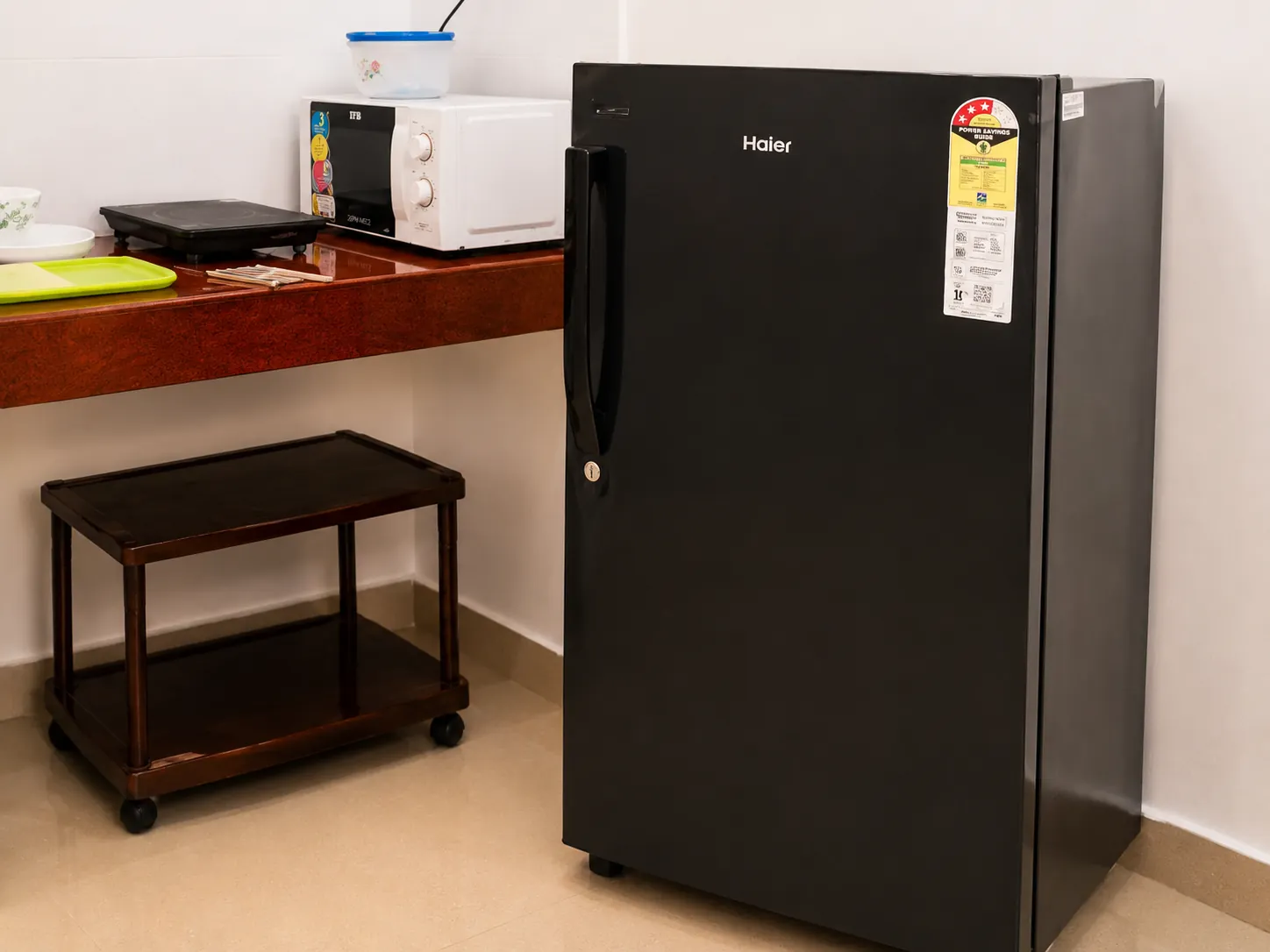 Refrigerator beside kitchen counter, microwave and trolley.