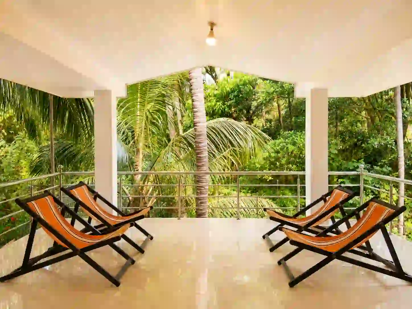 Covered balcony with four reclining chairs and greenery at Balakrishna Udupi Homestay.